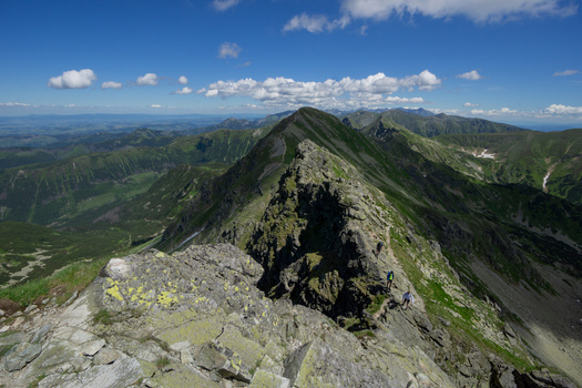 View of hikers on the rocky ridge of Tri kopy in Western Tatras with green mountain slopes under a blue sky in Ziar Zilina Region Slovakia. View of hikers on the rocky ridge of Tri kopy in Western Tatras with green mountain slopes under a blue sky in Ziar Zilina Region Slovakia.