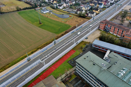 Aerial view of railway tracks with sound barriers running past a red running track and modern buildings in Forchheim Bavaria Germany.
