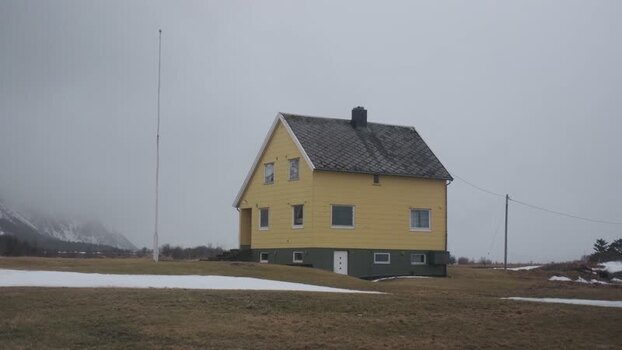 View of a yellow house and flagpole near mountains Norway.