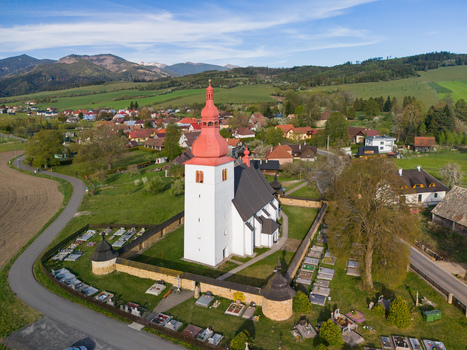 Aerial view of the Church of St. Ladislaus with its red onion dome and stone fortification wall surrounded by a cemetery and green hills in Liptovske Matiasovce Zilina Region Slovakia.