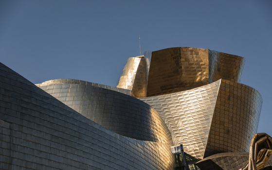 View of the shimmering titanium curves and metallic architecture of the Guggenheim Museum Bilbao under a clear blue sky in Bilbao Euskadi Spain. View of the shimmering titanium curves and metallic architecture of the Guggenheim Museum Bilbao under a clear blue sky in Bilbao Euskadi Spain.