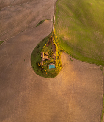 Aerial view of a farmhouse with a swimming pool surrounded by rolling hills in the golden light of sunset in Asciano Tuscany Italy.