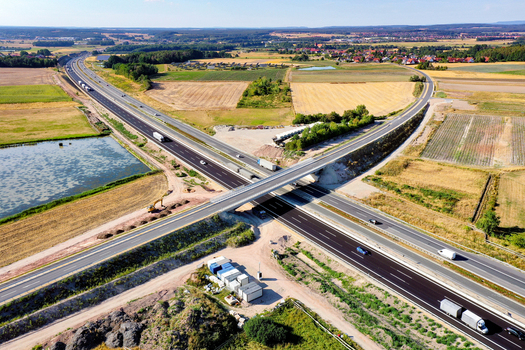Aerial view of the A73 highway interchange with trucks and cars driving through agricultural fields and construction zones Nurnberg Bayern Germany. Aerial view of the A73 highway interchange with trucks and cars driving through agricultural fields and construction zones Nurnberg Bayern Germany.