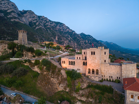 Aerial view of Kruje Castle with its historic stone walls and clock tower set against the rugged Skanderbeg Mountains under a clear blue sky Kruje Durres County Albania.