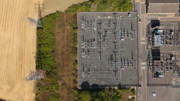 Aerial view of Eaton Socon Substation with electrical infrastructure transformers and power lines adjacent to a harvested field and green vegetation in St. Neots England United Kingdom. Aerial view of Eaton Socon Substation with electrical infrastructure transformers and power lines adjacent to a harvested field and green vegetation in St. Neots England United Kingdom.