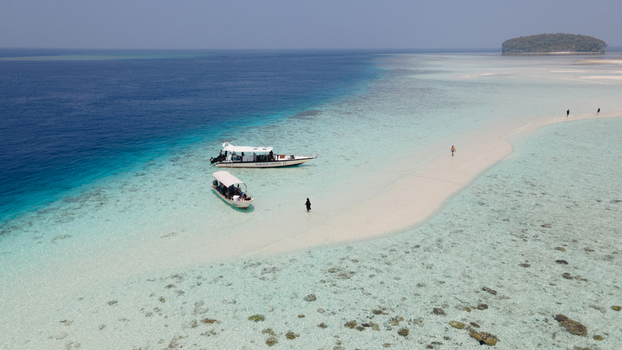 Aerial view of Raja Ampat featuring boats anchored near a pristine white sandbar surrounded by shallow turquoise water and coral reefs in Raja Ampat Southwest Papua Indonesia. Aerial view of Raja Ampat featuring boats anchored near a pristine white sandbar surrounded by shallow turquoise water and coral reefs in Raja Ampat Southwest Papua Indonesia.