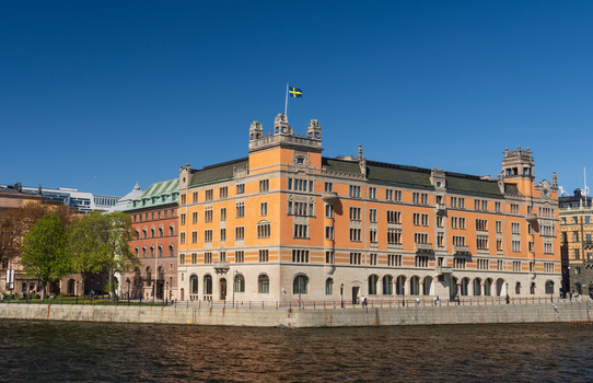 Stockholm Sweden 02 May 2026 View of Rosenbad building with its orange facade and Swedish flag by the Norrstrom river under a clear blue sky.