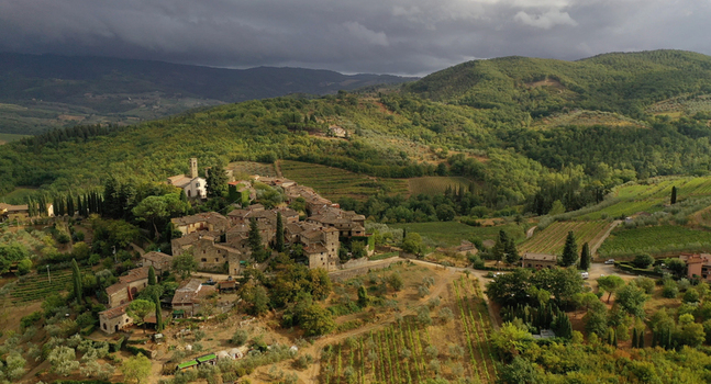 Aerial view of the historic stone village of Montefioralle nestled among rolling hills lush vineyards and olive groves under a dramatic sky in Greve in Chianti Tuscany Italy. Aerial view of the historic stone village of Montefioralle nestled among rolling hills lush vineyards and olive groves under a dramatic sky in Greve in Chianti Tuscany Italy.