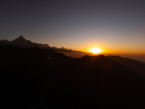 Aerial view of the Himalayan mountain range at sunrise with silhouetted peaks and a golden glow on the horizon in Nepal.