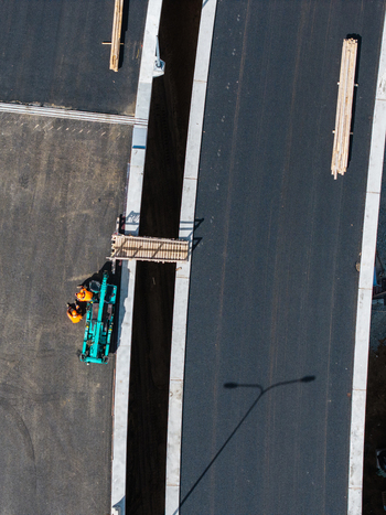 Aerial view of road construction workers in orange safety vests operating machinery near a trench on a new road project in Riga Latvia. Aerial view of road construction workers in orange safety vests operating machinery near a trench on a new road project in Riga Latvia.