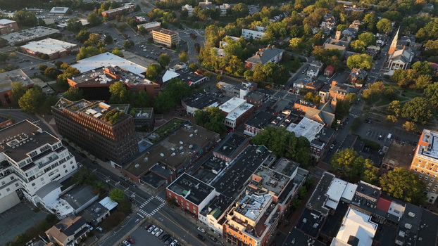 Aerial view of the historic downtown area featuring dense urban architecture tree lined streets and rooftops under warm afternoon light in Charlottesville Virginia United States.