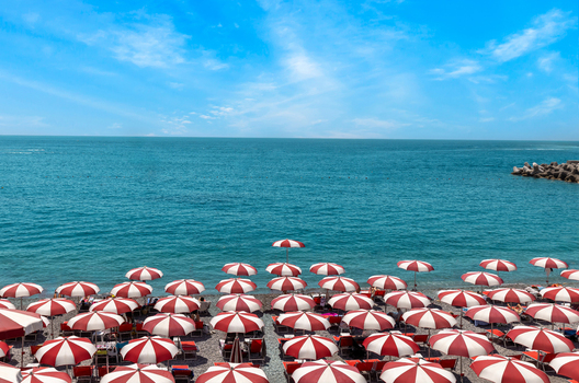Aerial view of the beach in Amalfi with numerous red and white striped umbrellas arranged on the shore along the blue Tyrrhenian Sea in Amalfi Campania Italy. Aerial view of the beach in Amalfi with numerous red and white striped umbrellas arranged on the shore along the blue Tyrrhenian Sea in Amalfi Campania Italy.