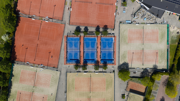 Aerial view of Tennis Padel Club Heiloo featuring red clay tennis courts and blue padel courts surrounded by lush green trees in Heiloo Noord Holland Netherlands.