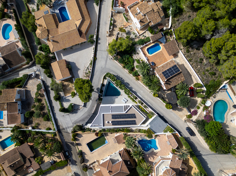 Aerial view of a modern villa with solar panels and a swimming pool surrounded by residential houses with pools and lush greenery in Moraira Valencian Community Spain.