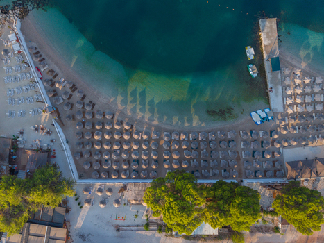 Aerial view of Ksamil beach featuring rows of sun loungers and umbrellas on the sand turquoise water a wooden pier and lush green trees in Ksamil Vlore County Albania. Aerial view of Ksamil beach featuring rows of sun loungers and umbrellas on the sand turquoise water a wooden pier and lush green trees in Ksamil Vlore County Albania.