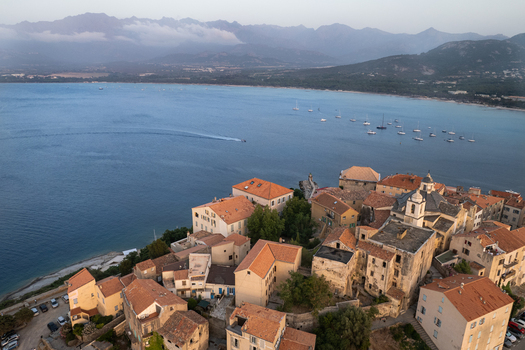 Aerial view of the historic Citadelle de Calvi with its stone buildings and terracotta rooftops overlooking the blue bay and mountains in Calvi Corse France.