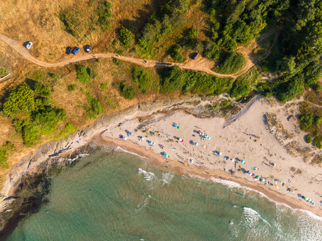 Aerial view of Coral Beach with colorful umbrellas on the sandy shore clear turquoise water and a dirt path winding through the grassy coastal hills in Tsarevo Burgas Bulgaria. Aerial view of Coral Beach with colorful umbrellas on the sandy shore clear turquoise water and a dirt path winding through the grassy coastal hills in Tsarevo Burgas Bulgaria.