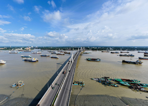 Aerial view of Shah Amanat Bridge spanning the Karnaphuli River with numerous cargo ships and boats in the water under a bright blue sky in Chattogram Chittagong Division Bangladesh.