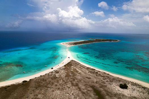 Aerial view of Los Roques archipelago featuring a white sandbar surrounded by turquoise Caribbean waters coral reefs and small boats in Los Roques Dependencias Federales Venezuela. Aerial view of Los Roques archipelago featuring a white sandbar surrounded by turquoise Caribbean waters coral reefs and small boats in Los Roques Dependencias Federales Venezuela.