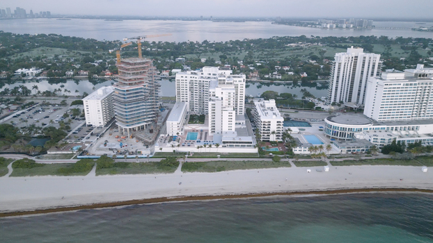Aerial view of the Miami Beach coastline featuring a high rise construction site with a crane luxury hotels swimming pools and sandy beach in Miami Beach Florida United States. Aerial view of the Miami Beach coastline featuring a high rise construction site with a crane luxury hotels swimming pools and sandy beach in Miami Beach Florida United States.