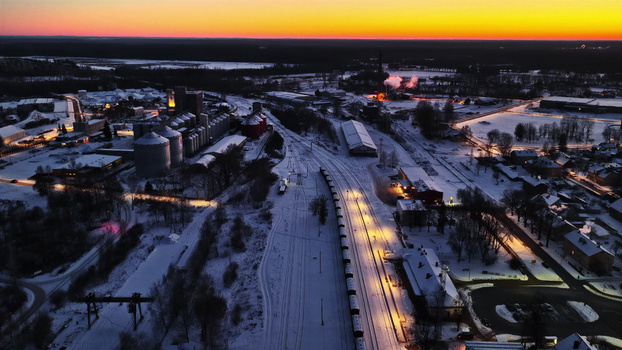 Aerial view of an industrial railway facility with grain silos and snow covered tracks illuminated by warm sunset light in Latvia. Aerial view of an industrial railway facility with grain silos and snow covered tracks illuminated by warm sunset light in Latvia.