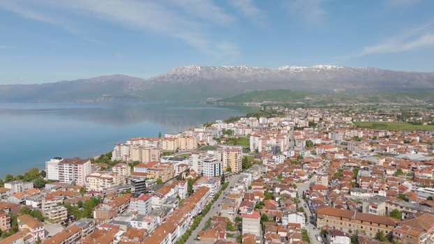 Aerial view of Pogradec city situated on the shore of Lake Ohrid with residential buildings rooftops and mountains in the background in Pogradec Korce County Albania. Aerial view of Pogradec city situated on the shore of Lake Ohrid with residential buildings rooftops and mountains in the background in Pogradec Korce County Albania.
