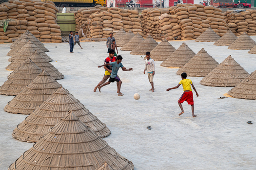 Brahmanbaria Bangladesh 24 January 2026 Aerial view of children playing football among conical bamboo covers and stacks of grain sacks in an open air processing yard.