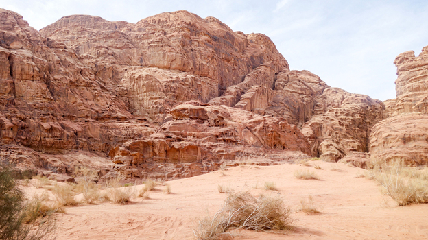 View of Wadi Rum Desert featuring towering sandstone rock formations and red sand dunes with sparse desert vegetation in Wadi Rum Village Aqaba Governorate Jordan. View of Wadi Rum Desert featuring towering sandstone rock formations and red sand dunes with sparse desert vegetation in Wadi Rum Village Aqaba Governorate Jordan.