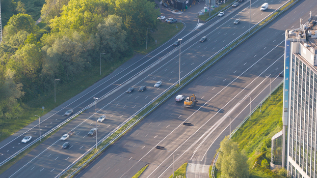 Waardenburg Netherlands 09 May 2026 Aerial view of the A2 motorway with cars driving past lush green trees and a modern office building under soft morning sunlight. Waardenburg Netherlands 09 May 2026 Aerial view of the A2 motorway with cars driving past lush green trees and a modern office building under soft morning sunlight.