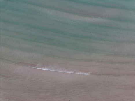 Aerial view of the turquoise waters of Gruinard Bay meeting the sandy shore with gentle ripples and a small breaking wave in Gruinard Scotland United Kingdom. Aerial view of the turquoise waters of Gruinard Bay meeting the sandy shore with gentle ripples and a small breaking wave in Gruinard Scotland United Kingdom.