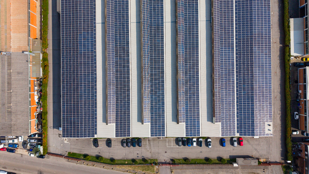 Aerial view of a large industrial facility featuring extensive rooftop solar panels a parking lot with parked cars and surrounding infrastructure in Milan Lombardy Italy.