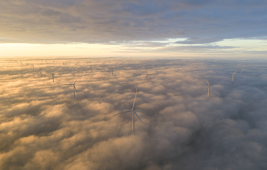 Aerial view of Windpark Fryslan wind turbines rising above a dense layer of clouds during a golden sunrise in Breezanddijk Friesland Netherlands.