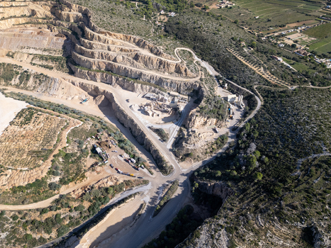 Aerial view of a large open pit quarry with terraced rock faces heavy machinery and winding access roads surrounded by Mediterranean landscape in Teulada Valencian Community Spain.