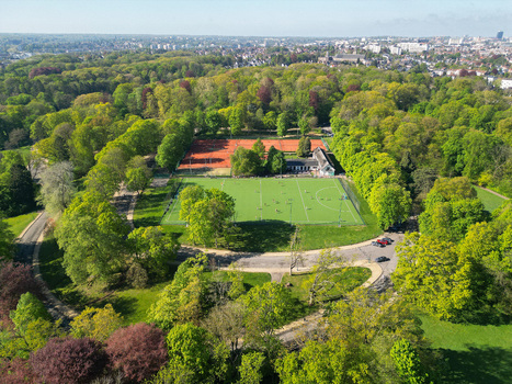 Aerial view of a sports complex with a green hockey field and red clay tennis courts surrounded by lush trees in a park Woluwe Saint Pierre Bruxelles Belgium. Aerial view of a sports complex with a green hockey field and red clay tennis courts surrounded by lush trees in a park Woluwe Saint Pierre Bruxelles Belgium.