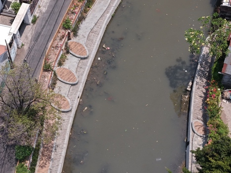 Aerial view of a canal flowing through an urban area with paved walkways wooden seating areas and lush vegetation in Kecamatan Denpasar Barat Bali Indonesia. Aerial view of a canal flowing through an urban area with paved walkways wooden seating areas and lush vegetation in Kecamatan Denpasar Barat Bali Indonesia.
