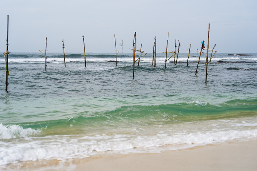 View of traditional stilt fishing poles standing in the turquoise ocean waves near a sandy beach Koggala Southern Province Sri Lanka. View of traditional stilt fishing poles standing in the turquoise ocean waves near a sandy beach Koggala Southern Province Sri Lanka.