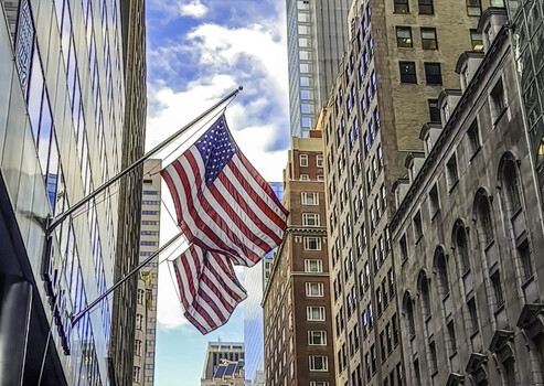 View of American flags hanging between historic and modern buildings in the urban canyon of New York New York United States.