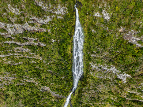 Aerial view of a vibrant waterfall cascades down the rugged verdant cliffs creating a mesmerizing contrast of white water against the lush greenery Faj&atilde; Grande Azores Portugal.