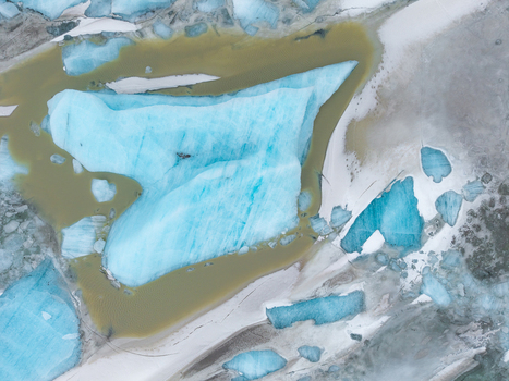 Aerial view of turquoise ice formations contrasting with the beige meltwater and the stark white surroundings creating a surreal landscape &Ouml;r&aelig;fi Iceland.