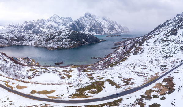 Aerial view of Lofoten with snow covered mountains a winding coastal road and a calm fjord in Nordland Norway.