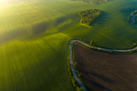 Aerial view of rolling green fields and a winding road through the countryside during golden hour in Kyjov South Moravian Region Czechia.
