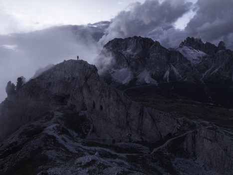 Aerial view of Croda Negra mountain peak with a person in a red jacket standing on a rocky ridge at Passo Falzarego Veneto Italy.