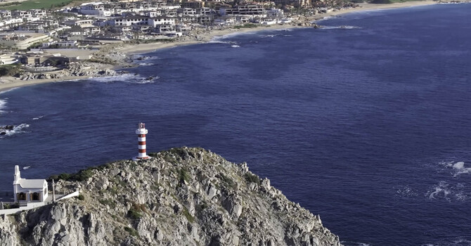 Aerial view of the red and white striped lighthouse on a rocky cliff overlooking the ocean with the town of Cabo San Lucas in the background Cabo San Lucas Baja California Sur Mexico.