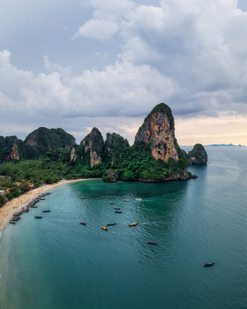 Aerial view of Railay Beach with its iconic limestone cliffs turquoise water and traditional long tail boats anchored along the sandy shore in Ao Nang Krabi Thailand. Aerial view of Railay Beach with its iconic limestone cliffs turquoise water and traditional long tail boats anchored along the sandy shore in Ao Nang Krabi Thailand.