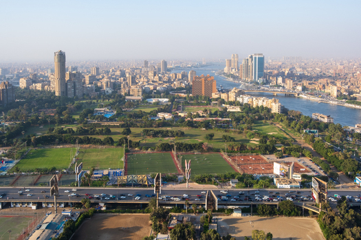 View of vibrant green spaces and buildings nestled along the Nile with a bustling highway below all under a hazy sky Zamalek Cairo Governorate Egypt. View of vibrant green spaces and buildings nestled along the Nile with a bustling highway below all under a hazy sky Zamalek Cairo Governorate Egypt.