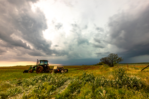 View of a tractor working in a field under a dramatic dark stormy sky with heavy clouds suggesting an approaching storm in Oklahoma City Oklahoma United States.
