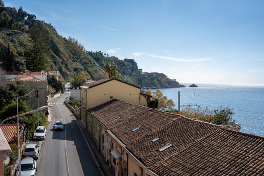 View of the azure sea meets the rugged coastline a winding road cutting through the quaint buildings and lush greenery under a clear sky Taormina Sicily Italy. View of the azure sea meets the rugged coastline a winding road cutting through the quaint buildings and lush greenery under a clear sky Taormina Sicily Italy.