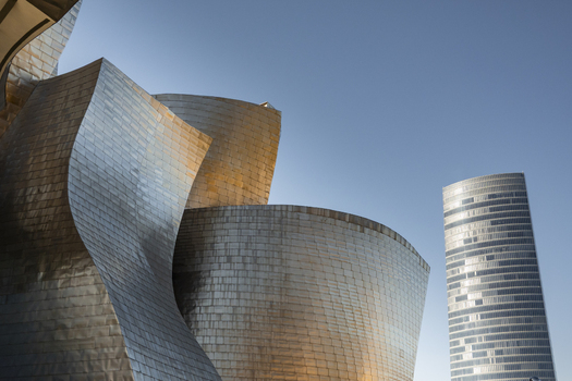 View of the Guggenheim Museum Bilbao featuring shimmering titanium panels and curved architectural lines with the Iberdrola Tower under a clear blue sky Bilbao Euskadi Spain. View of the Guggenheim Museum Bilbao featuring shimmering titanium panels and curved architectural lines with the Iberdrola Tower under a clear blue sky Bilbao Euskadi Spain.
