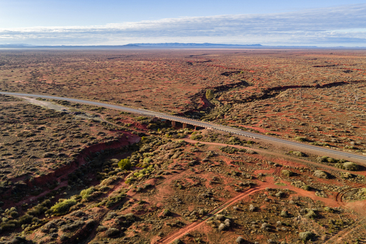 Aerial view of a long straight road crossing a bridge over a dry red creek bed in the vast outback landscape under a clear sky Flinders Ranges South Australia Australia.