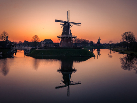 Aerial view of a traditional Dutch windmill reflecting in the calm water of a canal during a vibrant sunset in Dokkum Friesland Netherlands. Aerial view of a traditional Dutch windmill reflecting in the calm water of a canal during a vibrant sunset in Dokkum Friesland Netherlands.